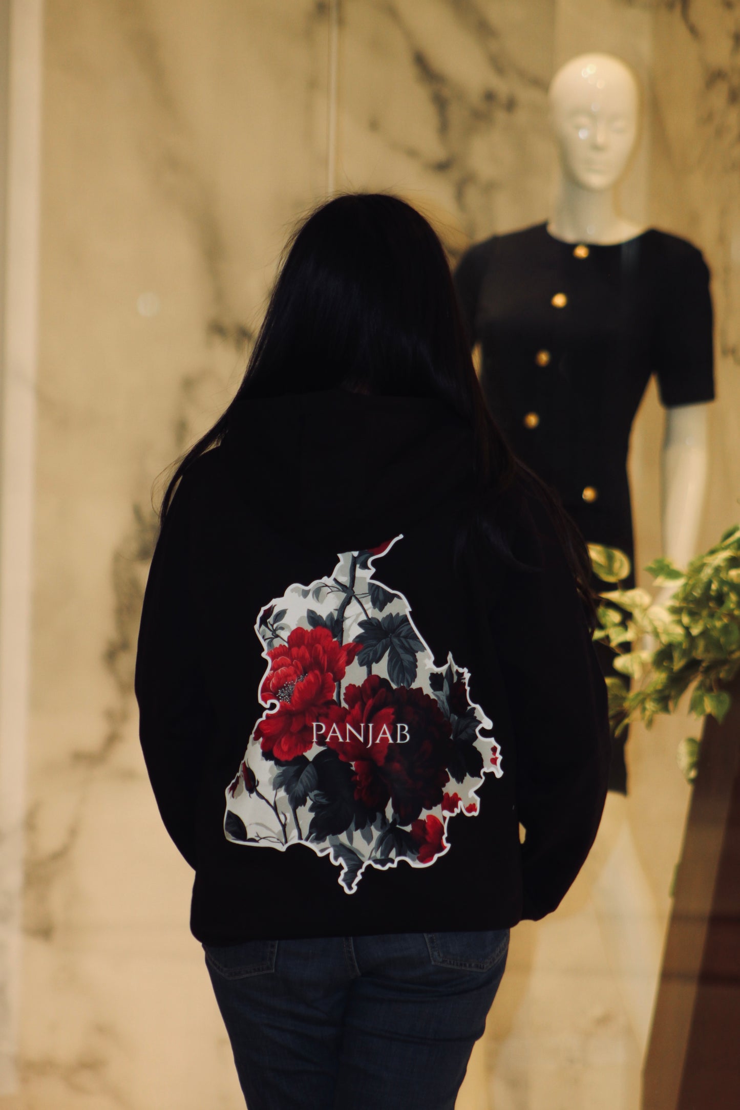 Person wearing a black hoodie with floral design and 'Panjab' text, standing in front of a mannequin.